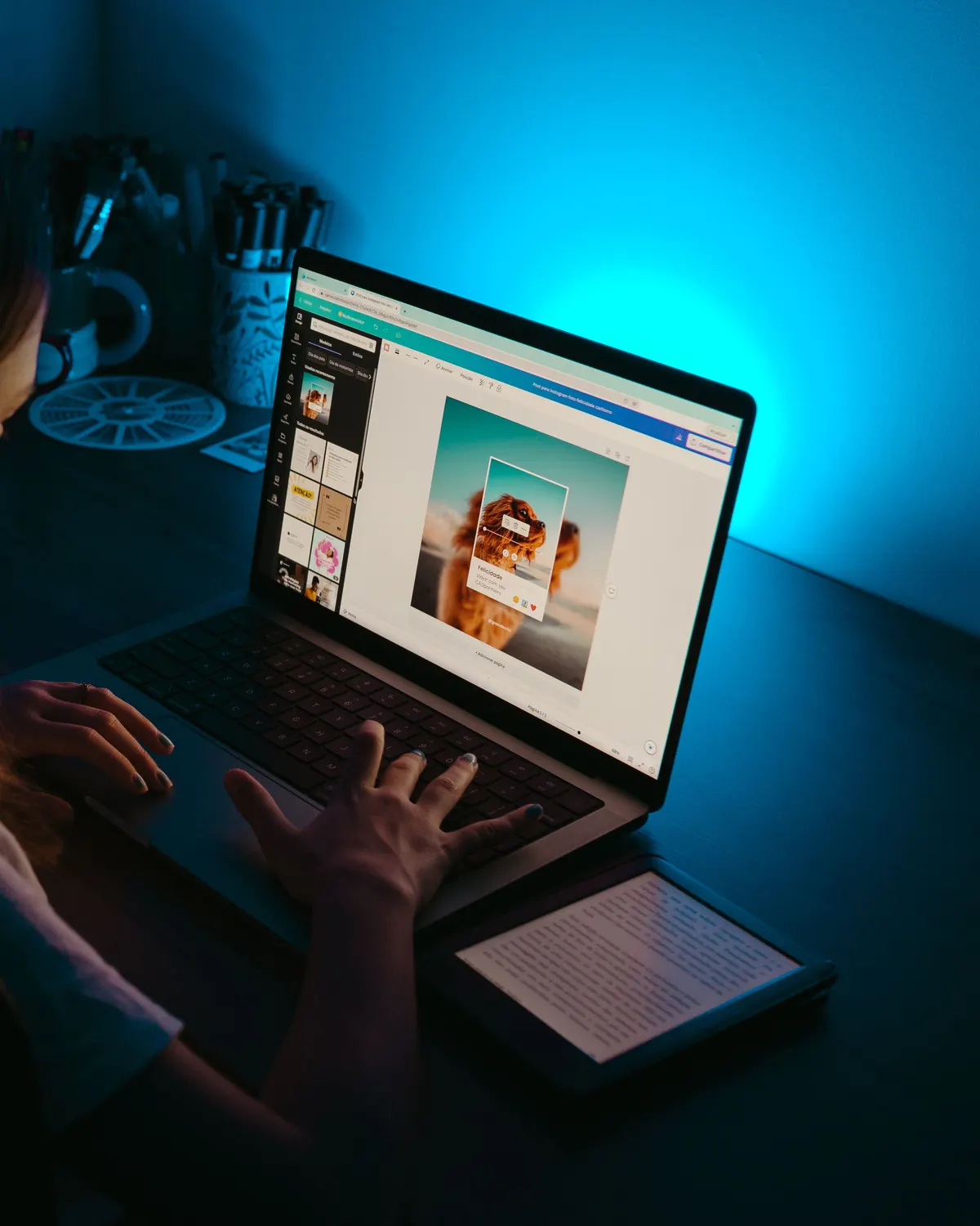 Manos sobre un portátil con un diseño en pantalla, bajo una luz azul